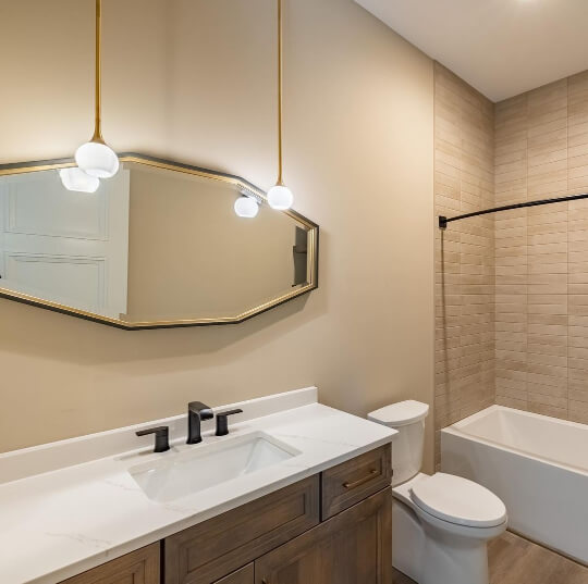 Sherwin Williams Shiitake on the walls in a bathroom with a long hexagon mirror hanging above an oak vanity with two pendant lights hanging from the ceiling.