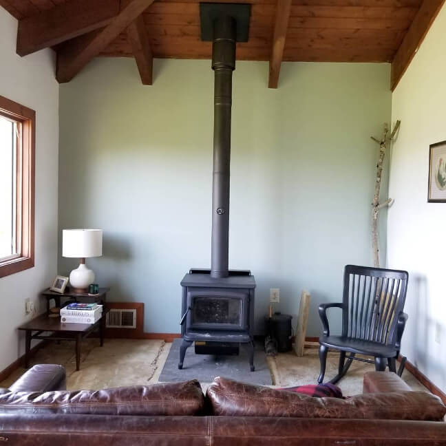 Benjamin Moore Misted Green, a dupe for Sherwin Williams Oyster Bay, on a feature wall in a cabin with cedar ceiling and black wood stove.