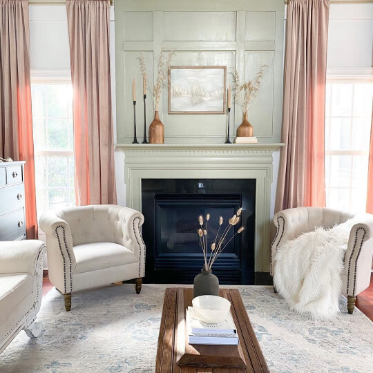 Sherwin Williams Svelte Sage on board and batten on a fireplace wall in a white living room with floor to ceiling pink curtains and plush white chairs