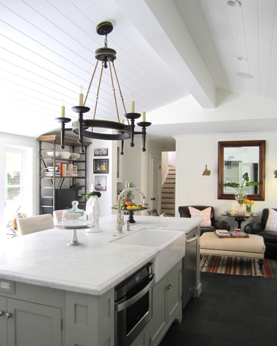 Benjamin Moore Fieldstone where it looks slightly green on a kitchen island in an otherwise white room with white marble counterops, silver hardware, and a black chandelier.
