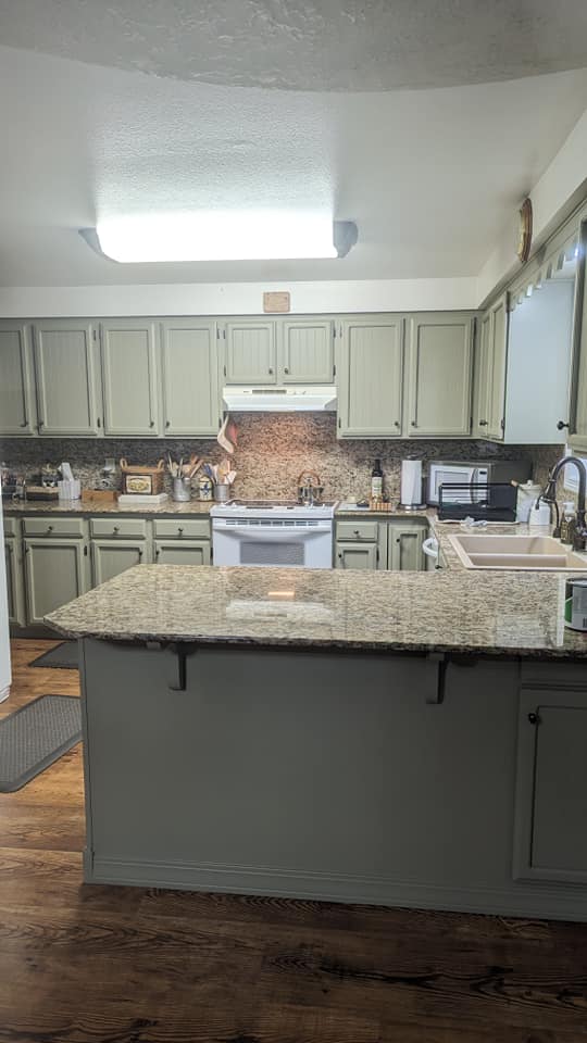 Benjamin Moore Dry Sage on all of the cabinets in a bright kitchen with warm granite countertops