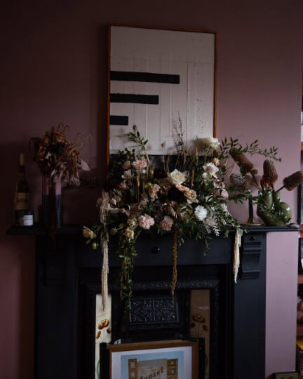 Sulking Room pink living room walls with dried flowers hanging off a blank fireplace.