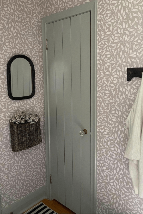 The sage green of fieldstone on trim and doors in a room with neutral leafy wallpaper
