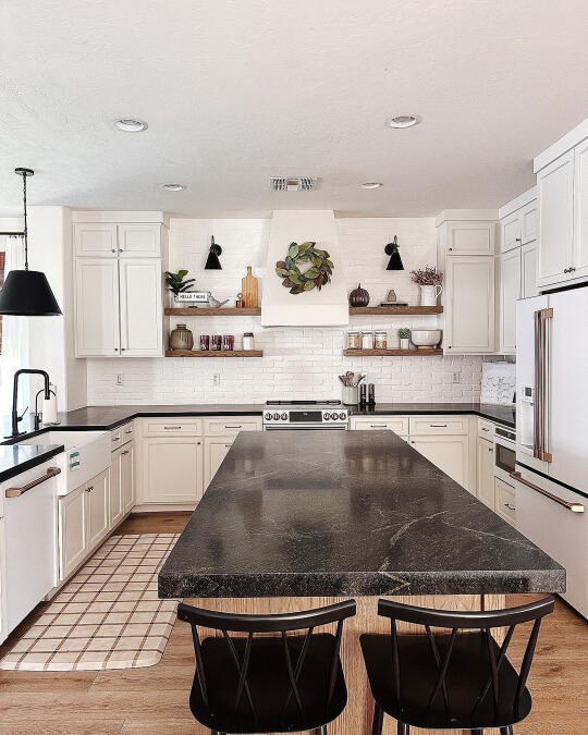 Sherwin Williams Aesthetic White on perimeter cabinets in a kitchen with white ceiling, brick backsplash, and black stone countertops, including over a large island in the center of the room.