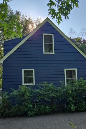 Side view of a small two storey cottage with siding freshly painted n Sherwin Williams Indigo Batik.