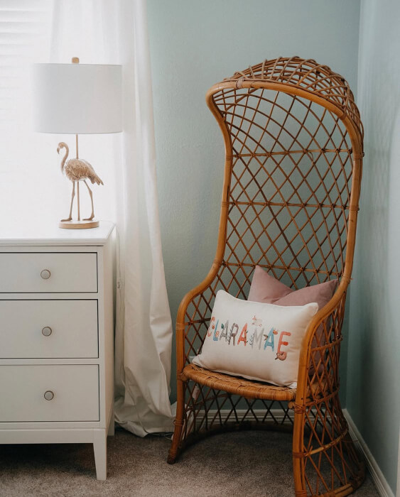 Sherwin Williams Rainwashed on a bedroom wall with a white cabinet, gold swan-shaped lamp, wicker chair with decorative pillows, and white curtains, shown in natural sunlight.