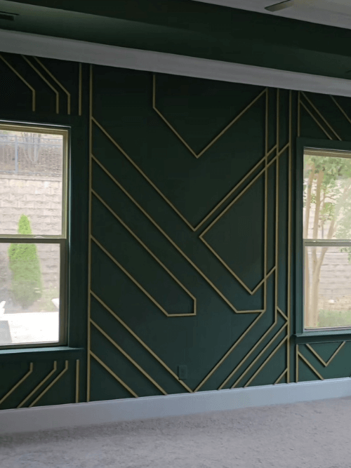 Sherwin Williams on all the walls in a living room with white trim and a metallic gold geometric design on the wall between two vertical windows.