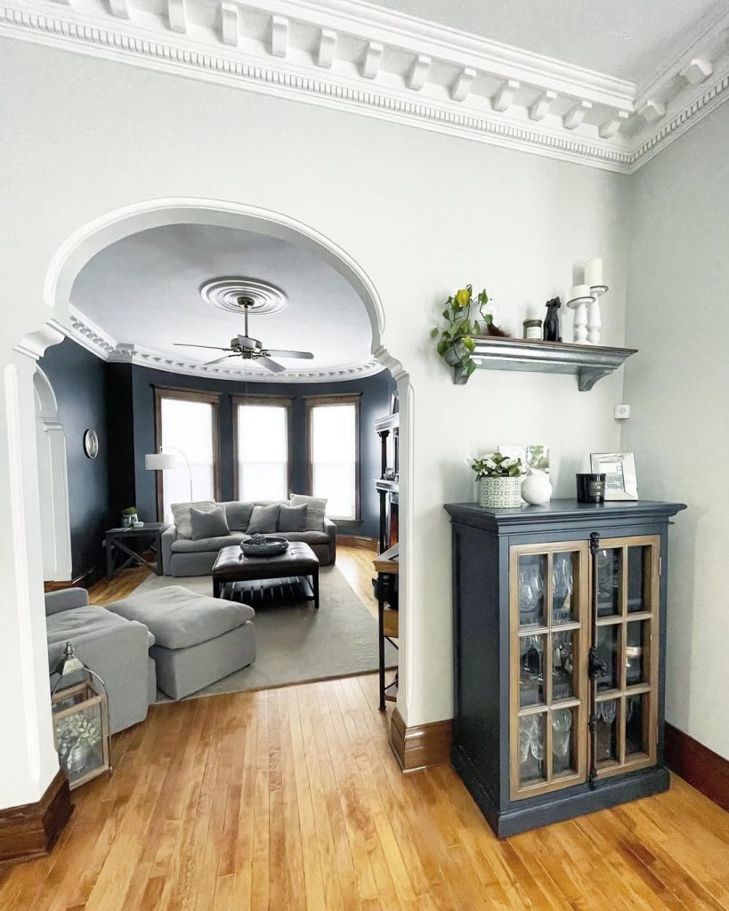 Benjamin Moore Moonshine in a living room  with white crown moulding and ceilings and an adjoining room in Benjamin Moore Soot.