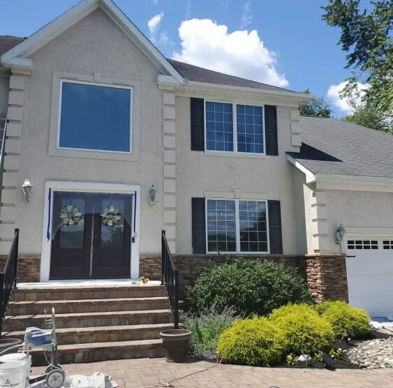 Benjamin Moore Revere Pewter Exterior of a two-story traditional home with a symmetrical façade, double front doors with glass panels, black shutters, a stone accent base along the lower portion, concrete steps leading to the entry, and landscaped shrubs in the front yard.