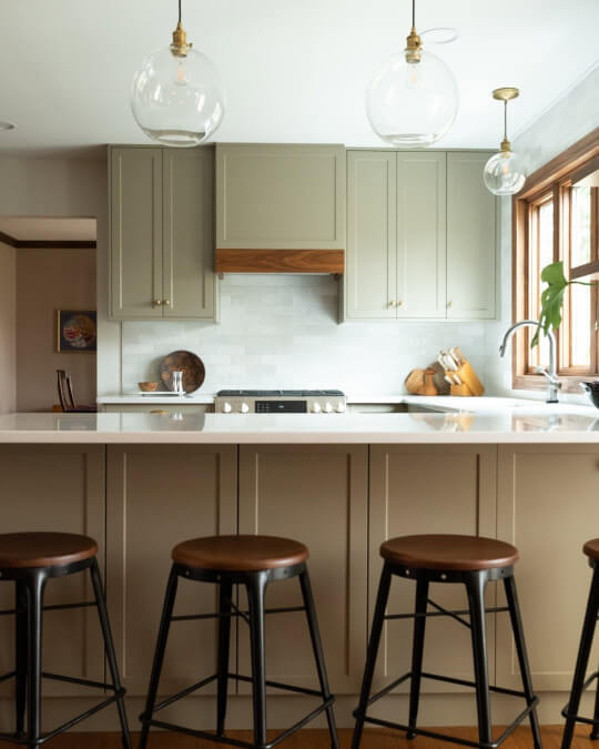 Semihandmade desert grey cabinets in a kitchen where the wall cabinets look green and the island looks brown.