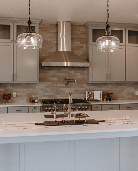 Evergreen Fog at 50% on kitchen cabinets with a textured stone backsplash, white stone countertops, and pendant lights.
