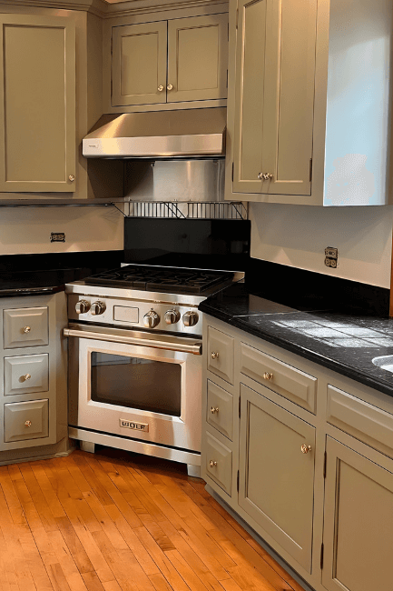 Sherwin Williams Evergreen Fog on cabinets in a medium sized L-shaped kitchen with black countertops.