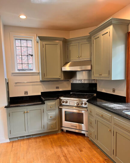 Sherwin Williams Evergreen Fog on cabinets in a medium sized L-shaped kitchen with black countertops.