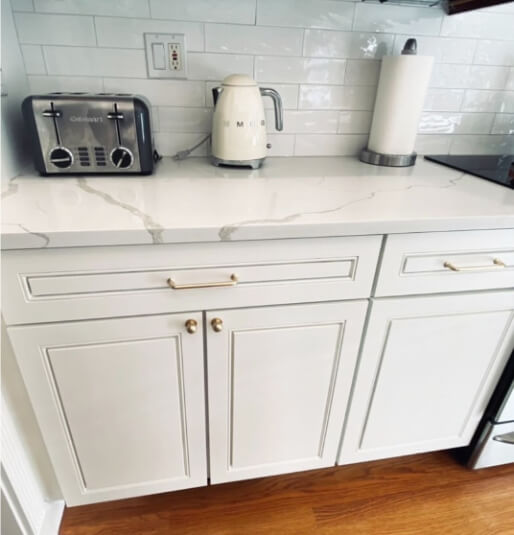 a custom color that looks like sherwin williams White Duck on kitchen cabinets with light stone countertops and white subway tile backsplash.