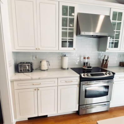A custom white color on kitchen cabinets that looks like Sherwin Williams White Duck, with stone countertops, white subway tile, and stainless oven and hood fan.