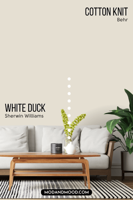 Sherwin Williams White Duck on one half of a wall and Behr dupe Cotton Knit on the other half in a living room behind a white sofa with a wood frame.