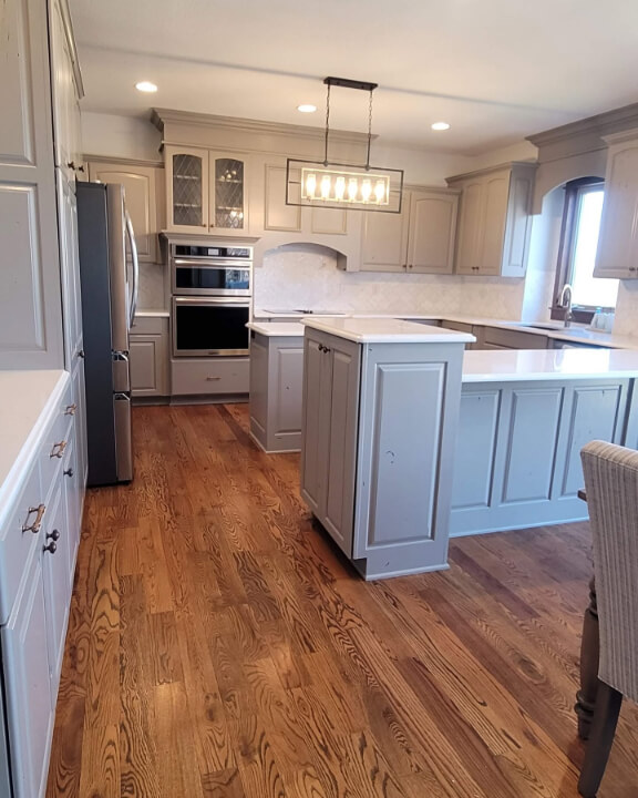 Sherwin Williams Pewter Tankard on cabinets where it looks blue, beige, and stony violet in different parts of the room with warm wood floors.